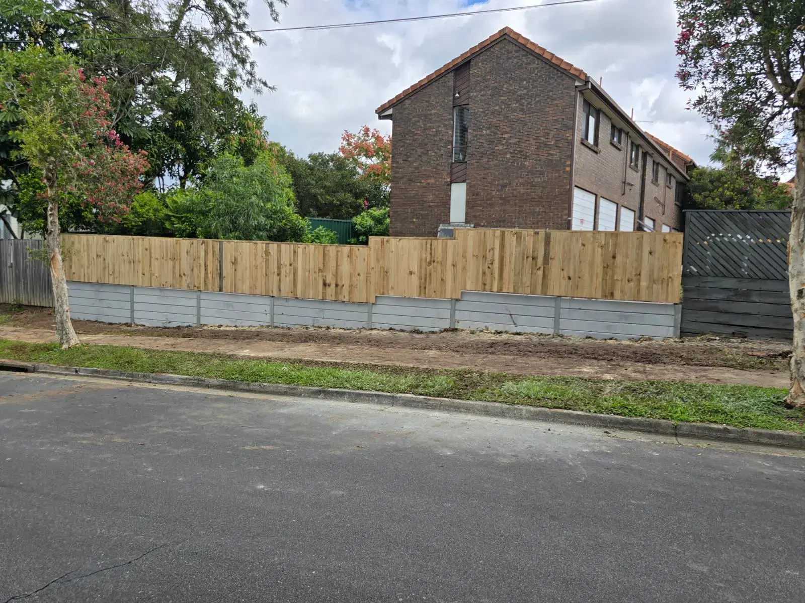 Concrete sleeper retaining wall with timber fencing above a street boundary